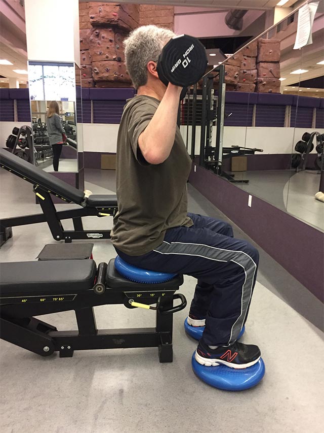 A man seated on an exercise bench lifts free weights.