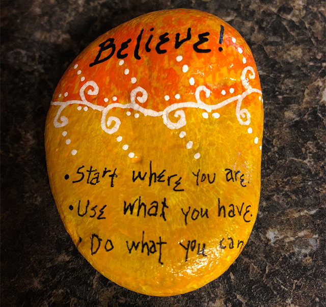 A brightly painted rock bears the words, Believe! Start where you are. Use what you have. Do what you can.