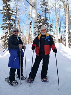 Two people in ski gear on a snowy, wooded mountain