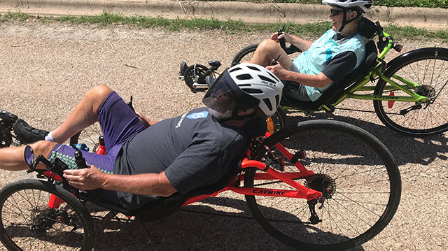 People in helmets on recumbent bikes , laying parallel to the road.