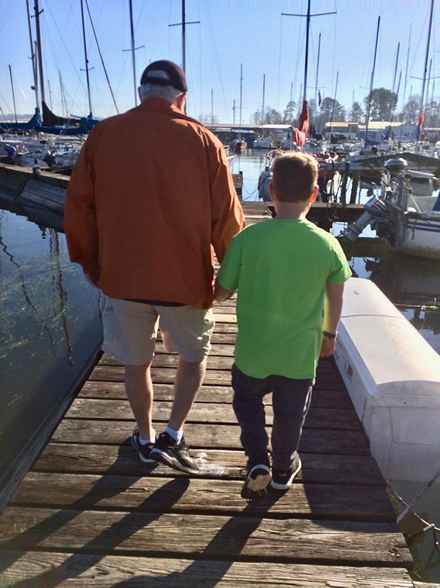 Senior man holding his grandson's hand on a boat dock.