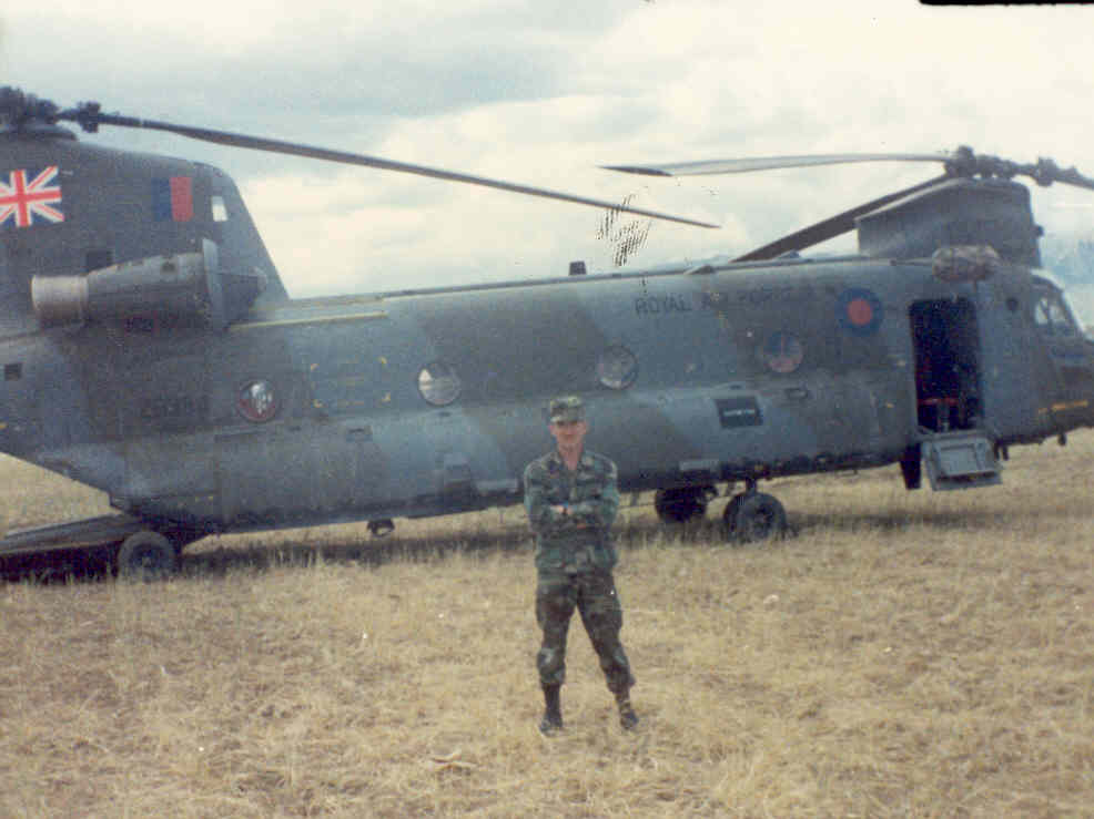 man pictured in front of military helicopter standing in grass with arms crossed 