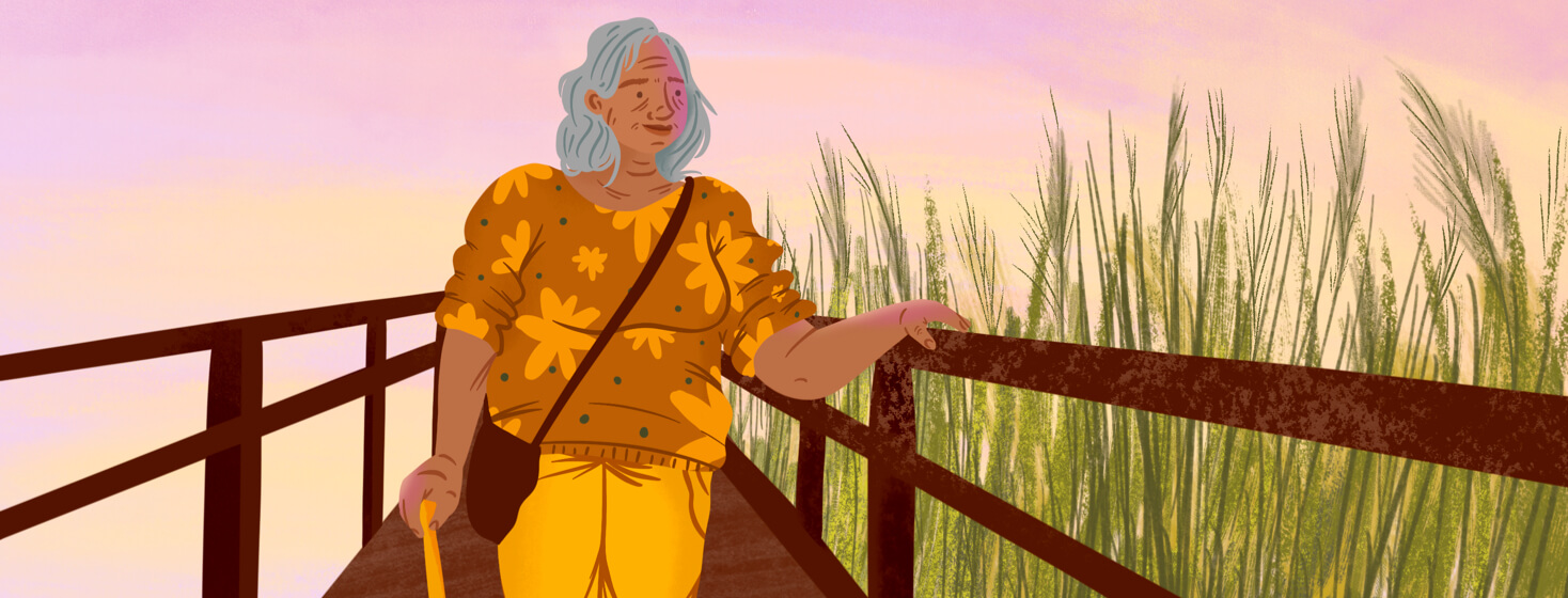Elder woman on a boardwalk with a walking cane smiles the sunset sky