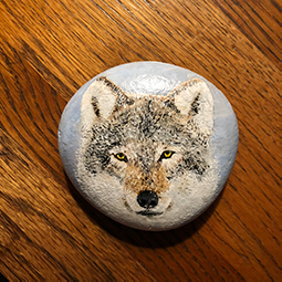 A smooth stone painted with a very detailed wolf head.