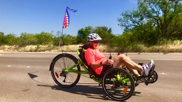 Photo of a smiling person on a recumbent bike on the road.